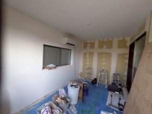 尼崎市で駐車場を部屋へリフォームした室内でクロスを施工している様子